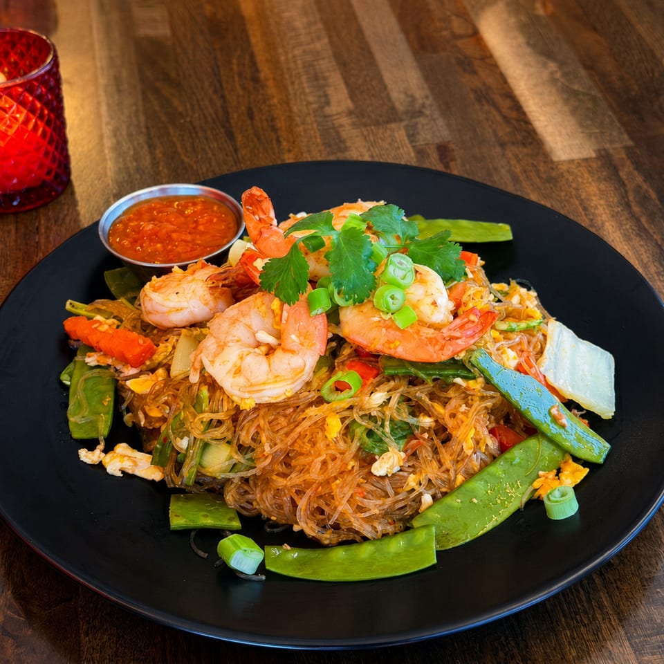 Glass noodles with shrimp, snow peas, carrots, and cilantro, served with a side of chili sauce.