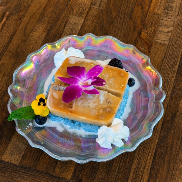 Two golden dessert bars with a purple orchid, blue rice, whipped cream, and berries on a iridescent plate.