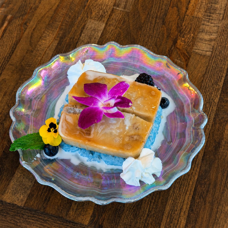 Two golden dessert bars with a purple orchid, blue rice, whipped cream, and berries on a iridescent plate.