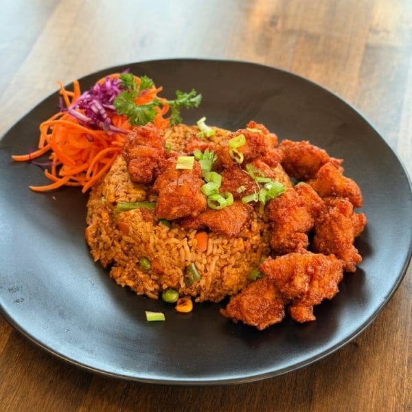 Fried rice with crispy orange chicken, garnished with green onions, shredded carrots, and red cabbage.