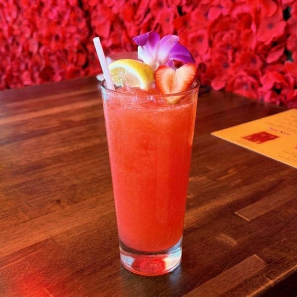 A vibrant red cocktail with a lemon slice, strawberry, and purple orchid on a wooden table.